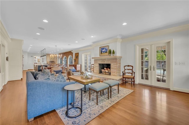 living room featuring french doors, crown molding, an inviting chandelier, and light wood-type flooring