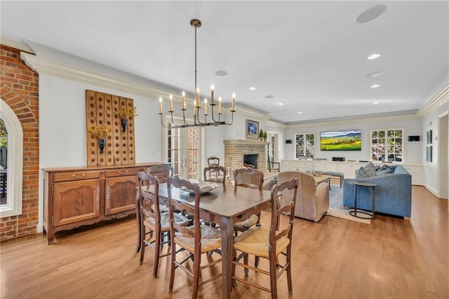 dining area featuring ornamental molding, light hardwood / wood-style flooring, a notable chandelier, and a fireplace