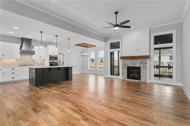 kitchen with pendant lighting, custom exhaust hood, an island with sink, white cabinetry, and light wood-type flooring