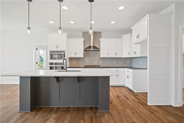 kitchen with wall chimney exhaust hood, light hardwood / wood-style floors, pendant lighting, white cabinetry, and appliances with stainless steel finishes