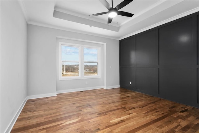 unfurnished bedroom featuring ornamental molding, a tray ceiling, hardwood / wood-style floors, and ceiling fan