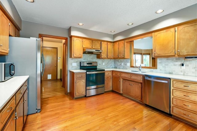 kitchen with appliances with stainless steel finishes, sink, a textured ceiling, light hardwood / wood-style floors, and decorative backsplash