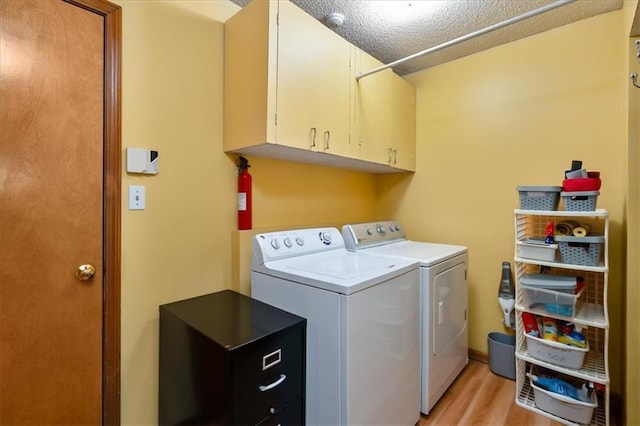 laundry area featuring a textured ceiling, light hardwood / wood-style flooring, cabinets, and washer and clothes dryer