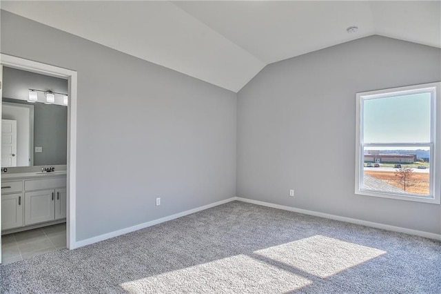 unfurnished bedroom featuring light carpet, lofted ceiling, and ensuite bathroom