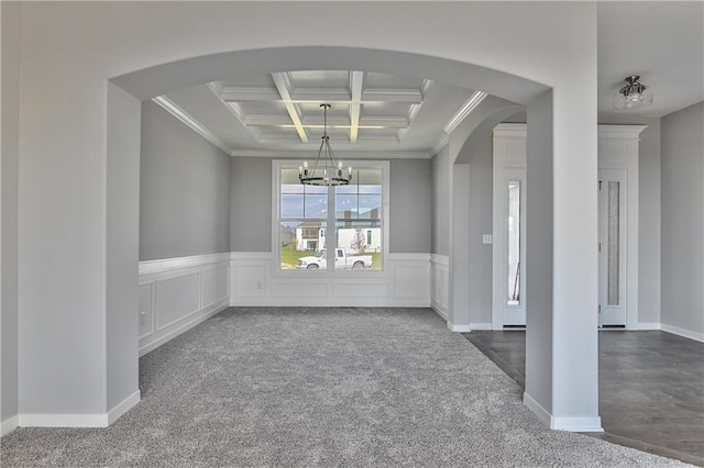 carpeted empty room featuring coffered ceiling, beam ceiling, crown molding, and an inviting chandelier