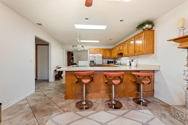 kitchen with stainless steel refrigerator with ice dispenser, kitchen peninsula, decorative light fixtures, a kitchen bar, and light tile patterned flooring