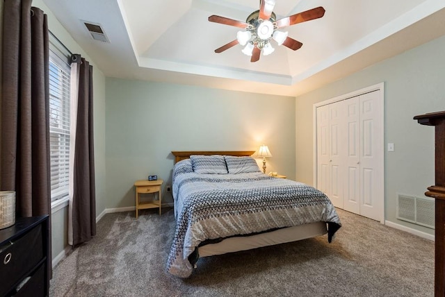 carpeted bedroom featuring a closet, a tray ceiling, and ceiling fan