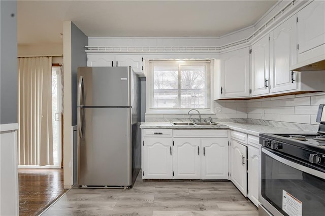 kitchen featuring decorative backsplash, stainless steel appliances, sink, light hardwood / wood-style flooring, and white cabinetry