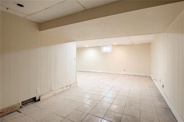 basement featuring a paneled ceiling and wooden walls