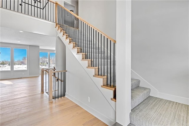stairs with wood finished floors, baseboards, and a towering ceiling