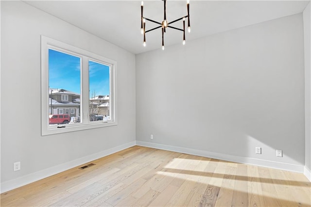 unfurnished room featuring a chandelier, wood finished floors, and baseboards