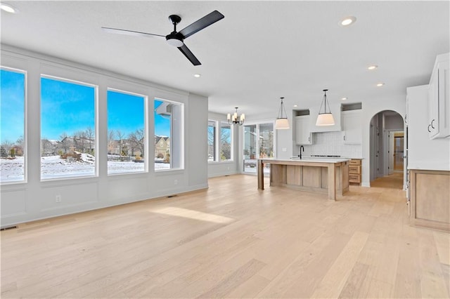 unfurnished living room with a ceiling fan, arched walkways, light wood finished floors, a sink, and a chandelier