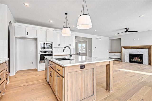 kitchen featuring appliances with stainless steel finishes, a sink, light wood-style floors, a textured ceiling, and a fireplace