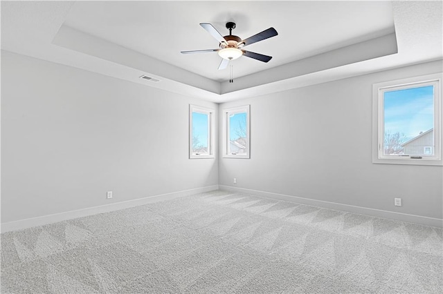 carpeted spare room featuring a raised ceiling, baseboards, and a ceiling fan