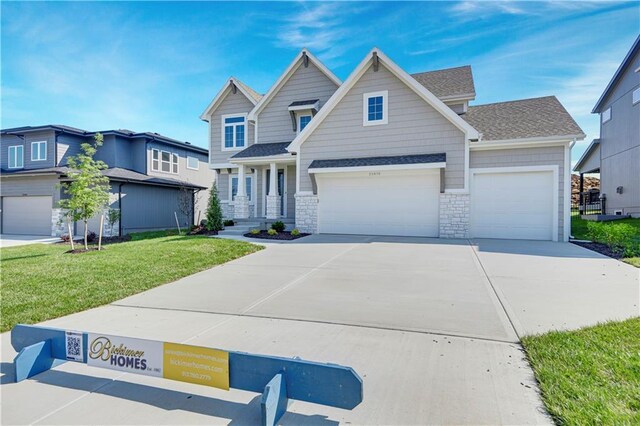 22070 W 100th Ter, Lenexa, KS 66220 - view of front of home with a front lawn, concrete driveway, an attached garage, stone siding, and a shingled roof