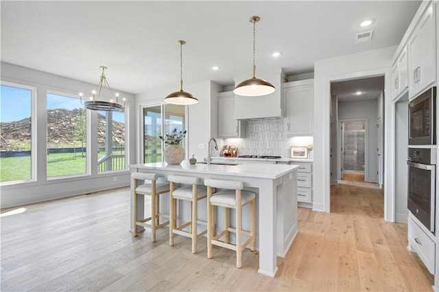 22070 W 100th Ter, Lenexa, KS 66220 - kitchen with appliances with stainless steel finishes, light wood-type flooring, light countertops, decorative backsplash, and a center island with sink