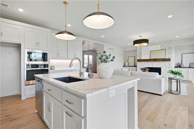 22070 W 100th Ter, Lenexa, KS 66220 - kitchen featuring appliances with stainless steel finishes, light wood-type flooring, white cabinets, a center island with sink, and hanging light fixtures
