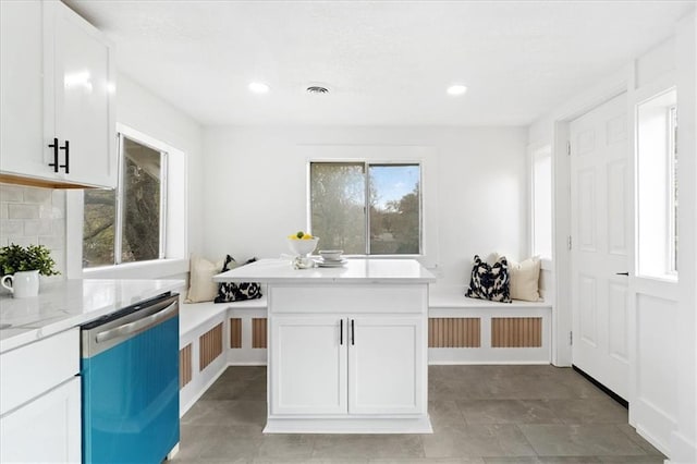 kitchen featuring decorative backsplash, light stone countertops, light tile patterned flooring, stainless steel dishwasher, and white cabinets