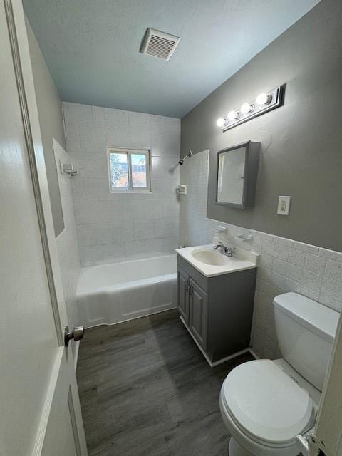 full bathroom with hardwood / wood-style floors, vanity, tile walls, tiled shower / bath combo, and toilet