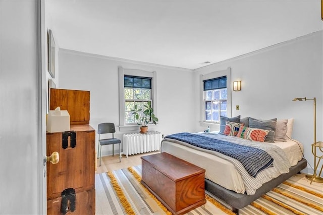 bedroom featuring radiator, ornamental molding, multiple windows, and light wood-type flooring