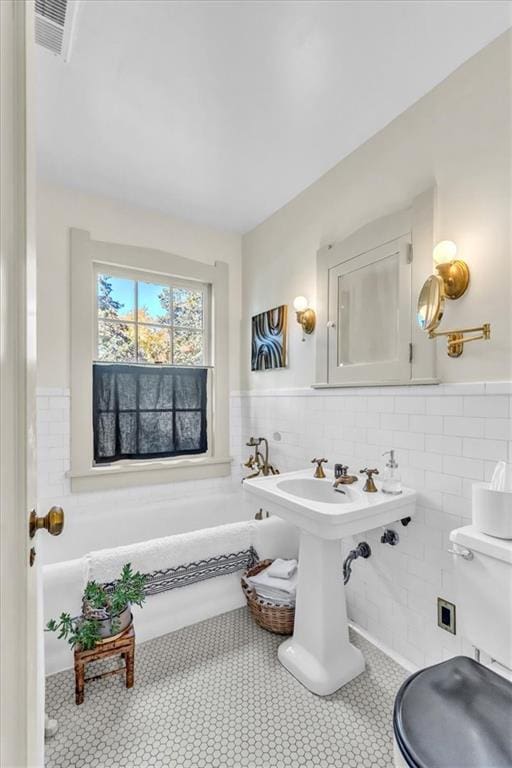 bathroom with tile walls, tile patterned floors, toilet, and a washtub