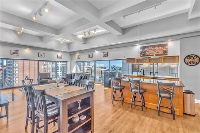 dining area featuring light wood-type flooring, beamed ceiling, track lighting, and sink