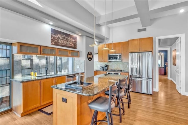 kitchen with hanging light fixtures, sink, backsplash, a kitchen island, and stainless steel appliances