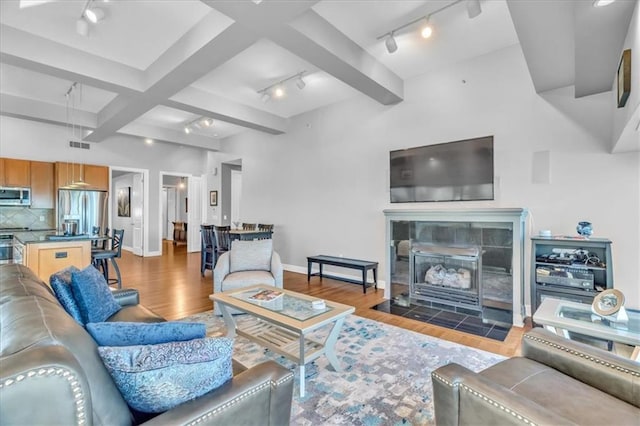 living room with a fireplace, rail lighting, light wood-type flooring, and beamed ceiling