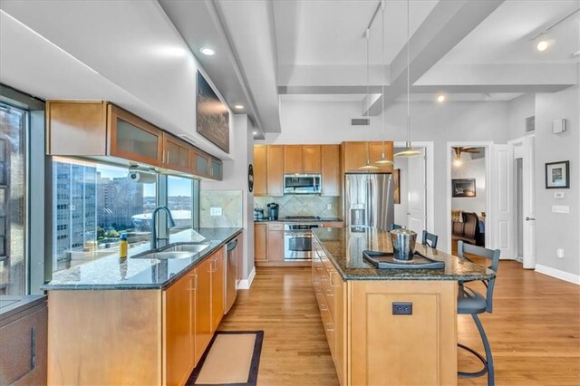 kitchen featuring a spacious island, decorative light fixtures, stainless steel appliances, sink, and light hardwood / wood-style flooring