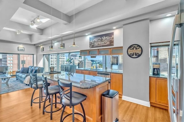 kitchen with a center island, sink, light wood-type flooring, dark stone counters, and a breakfast bar area