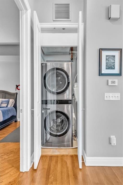 laundry area with stacked washer / dryer and light hardwood / wood-style flooring