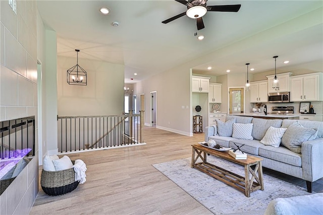 living room with ceiling fan with notable chandelier, light wood-type flooring, and a tiled fireplace