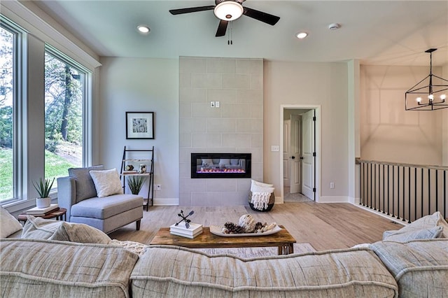 living room featuring ceiling fan with notable chandelier, a wealth of natural light, a tile fireplace, and light hardwood / wood-style flooring