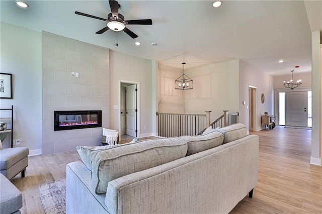 living room with ceiling fan with notable chandelier, light hardwood / wood-style flooring, and a tiled fireplace