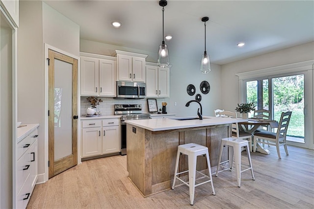 kitchen featuring light wood-type flooring, pendant lighting, a center island with sink, stainless steel appliances, and white cabinets