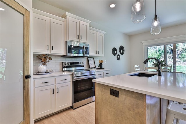 kitchen with light hardwood / wood-style floors, pendant lighting, sink, stainless steel appliances, and white cabinetry