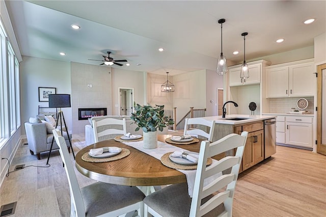 dining area with ceiling fan with notable chandelier, light hardwood / wood-style floors, a fireplace, and sink