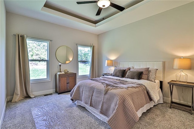 bedroom featuring ceiling fan, light colored carpet, and a tray ceiling