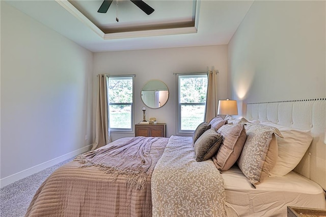 bedroom with ceiling fan, a tray ceiling, carpet flooring, and multiple windows