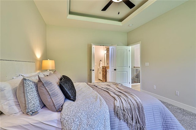 carpeted bedroom featuring a raised ceiling, ensuite bathroom, and ceiling fan