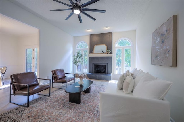 living room featuring wood-type flooring, a tiled fireplace, and ceiling fan