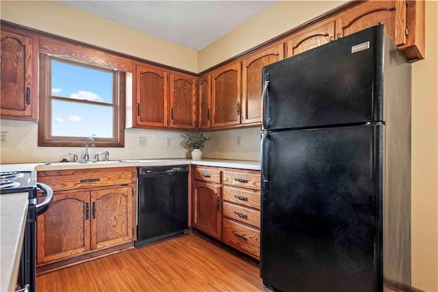 kitchen featuring black appliances, sink, light hardwood / wood-style floors, and a textured ceiling