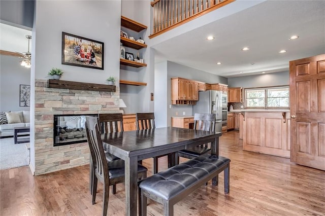 dining area with ceiling fan, a stone fireplace, and light hardwood / wood-style flooring