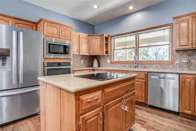 kitchen featuring appliances with stainless steel finishes, sink, a kitchen island, backsplash, and light hardwood / wood-style flooring