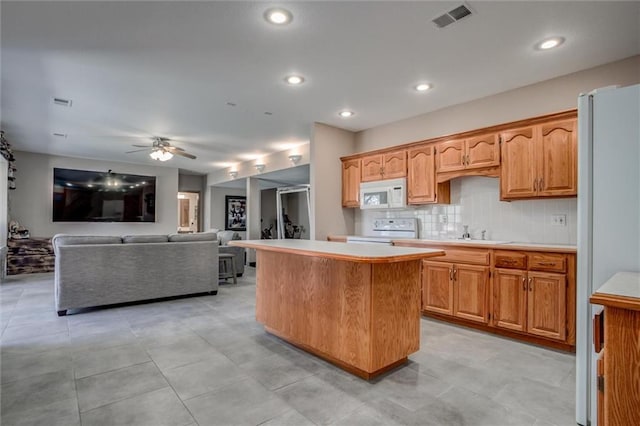 kitchen featuring tasteful backsplash, ceiling fan, sink, a center island, and white appliances