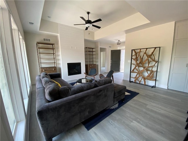 living room featuring a fireplace, a tray ceiling, light hardwood / wood-style flooring, and ceiling fan