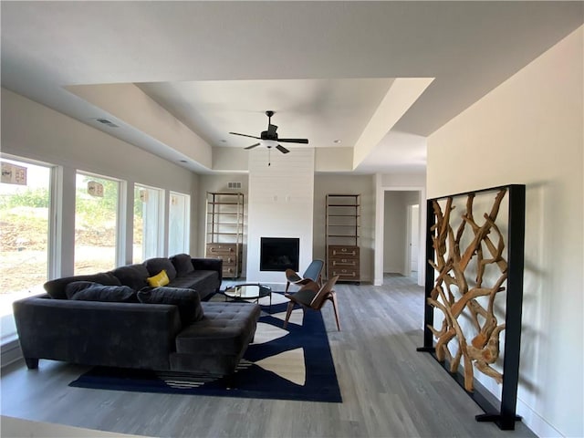 living room with ceiling fan, hardwood / wood-style flooring, a fireplace, and a tray ceiling