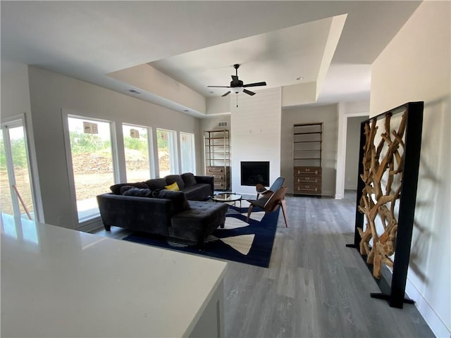 living room featuring hardwood / wood-style floors, ceiling fan, a tray ceiling, and a large fireplace