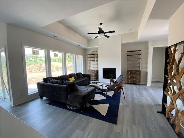 living room with ceiling fan, a fireplace, dark wood-type flooring, and a tray ceiling