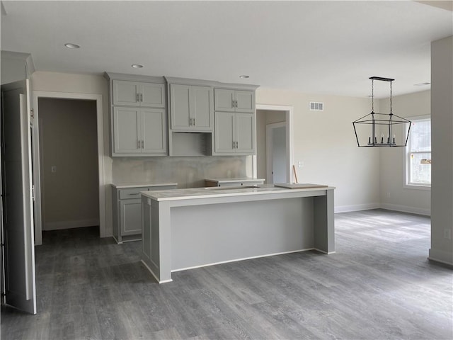 kitchen with gray cabinetry, dark hardwood / wood-style flooring, hanging light fixtures, an inviting chandelier, and a center island with sink